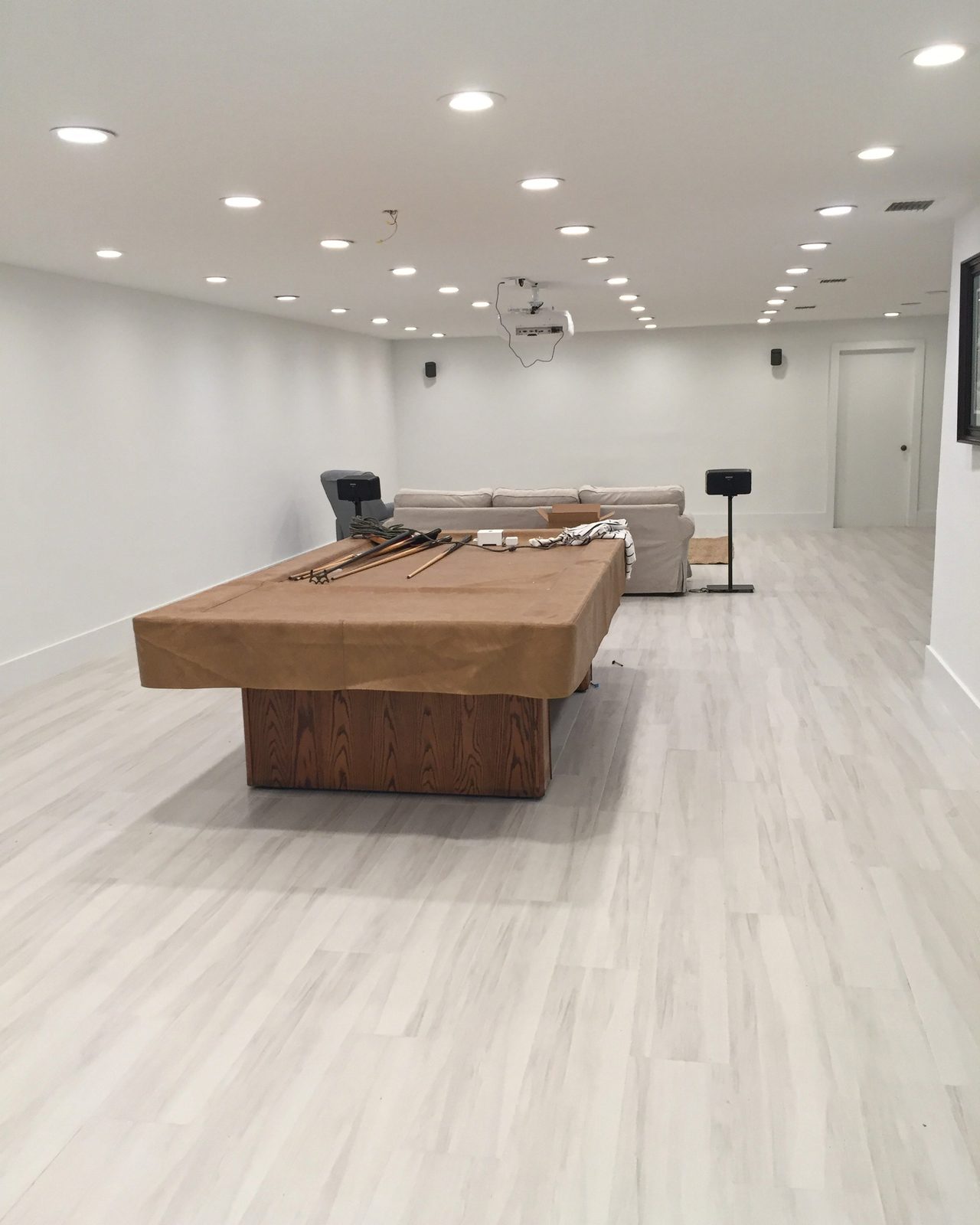 Finished basement with light plank flooring and recessed lighting