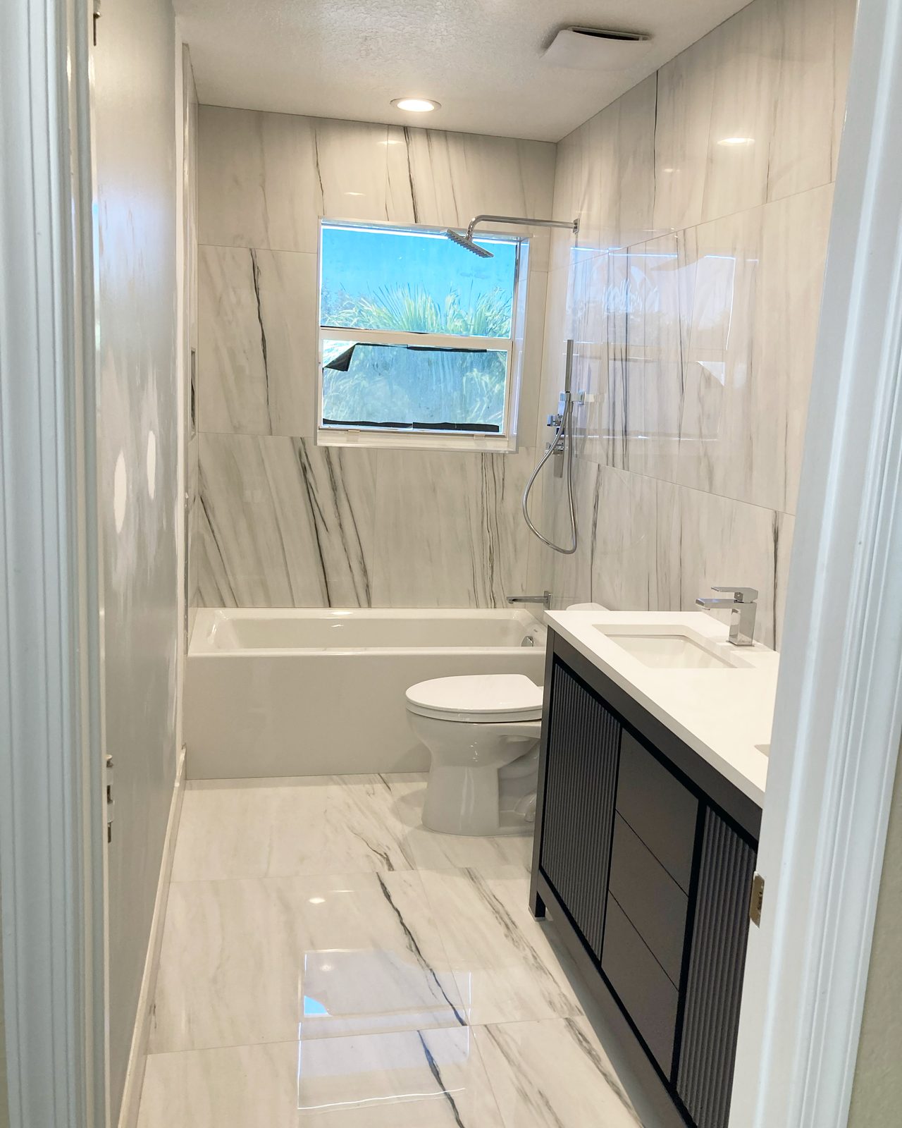 Remodeled bathroom with marble tile, soaking tub, and dark vanity