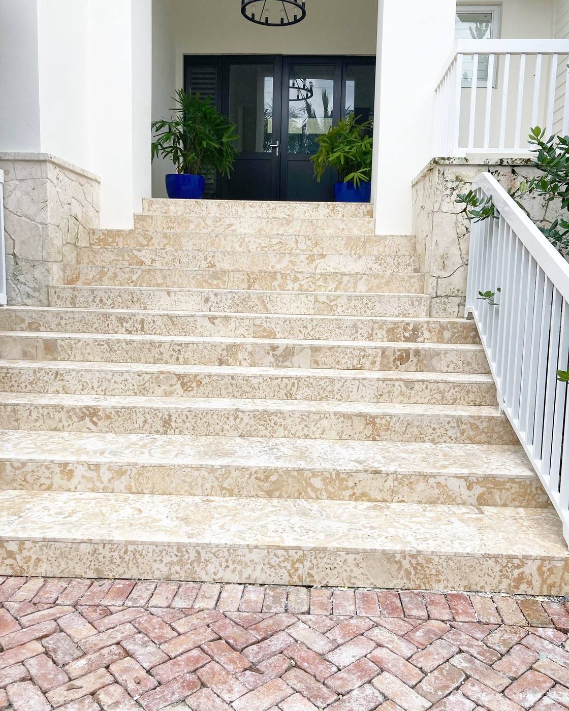 Coral stone entry steps with white railings and herringbone brick walkway